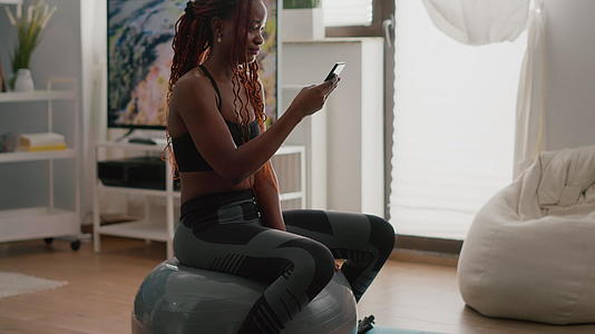 坐在健身球上的黑皮肤女人在电话里写信息视频的预览图