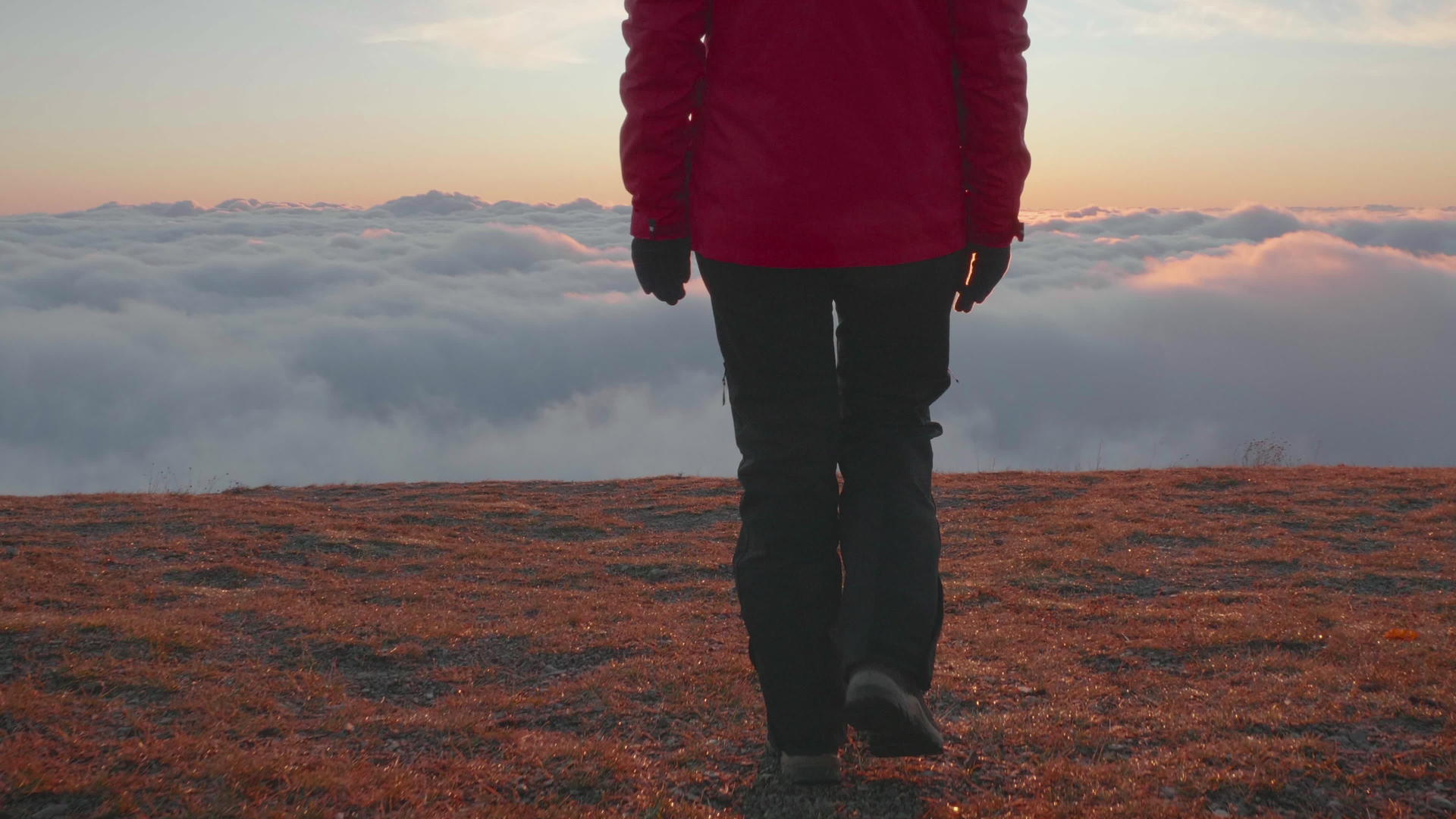 穿着夹克和裤子的年轻女子正步行到云端高山边缘视频的预览图