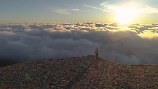 早上这位妇女站在山高原边缘靠近粉红色云朵上方的鸟瞰图视频的预览图
