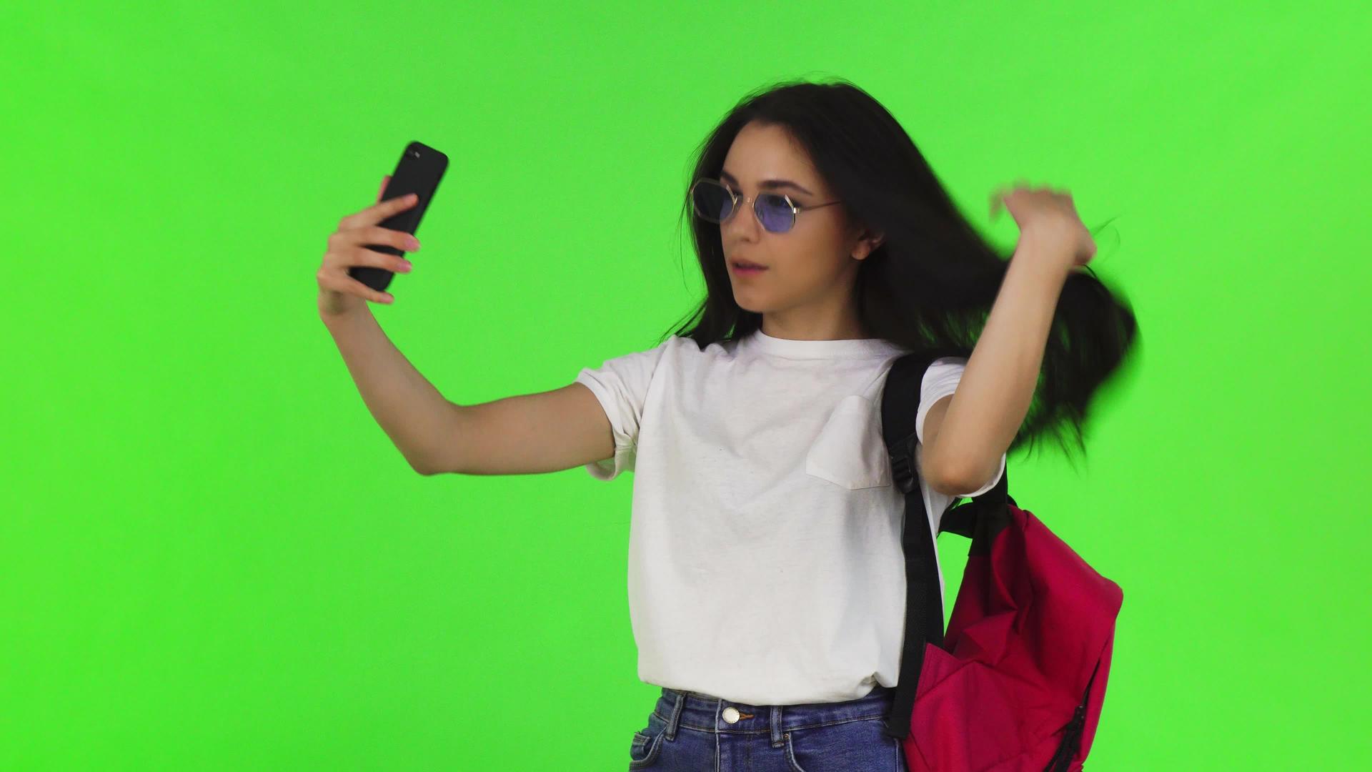 一个穿着背包的迷人女学生用她的智能手机自拍视频的预览图