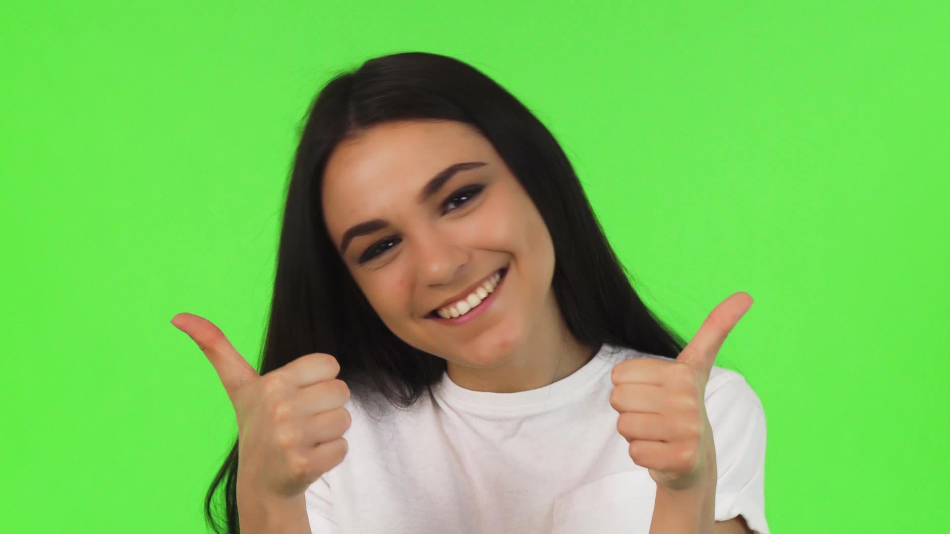 一个快乐的女孩竖起大拇指站在绿色的背景上视频的预览图