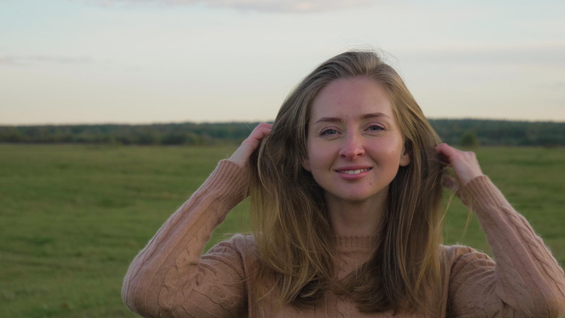 在绿色的田野里年轻快乐的女人微笑着摸着头发的肖像镜头慢动作视频的预览图