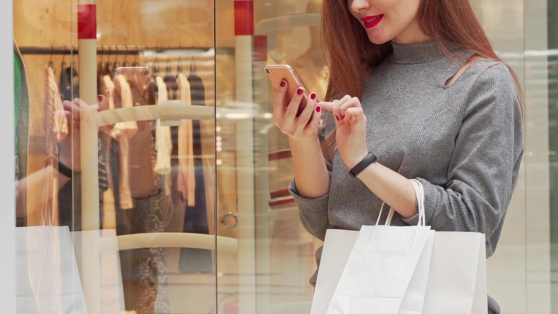 当一个女人在购物中心购物时她微笑着看着她的智能手机视频的预览图