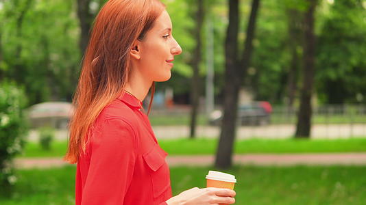 红发女商人喝卡布奇诺咖啡在户外散步视频的预览图
