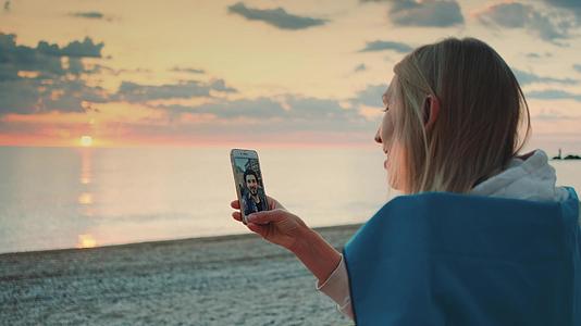年轻女子在海滩上用智能手机给朋友打视频电话视频的预览图