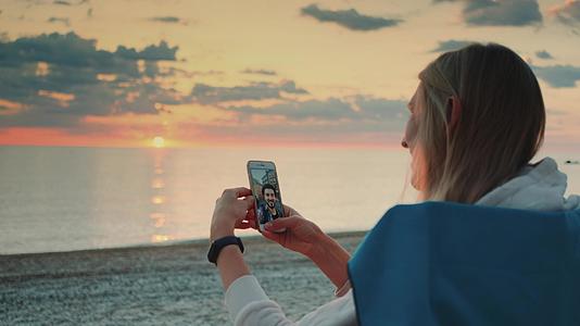 年轻女子在海滩上用智能手机给朋友打视频电话视频的预览图