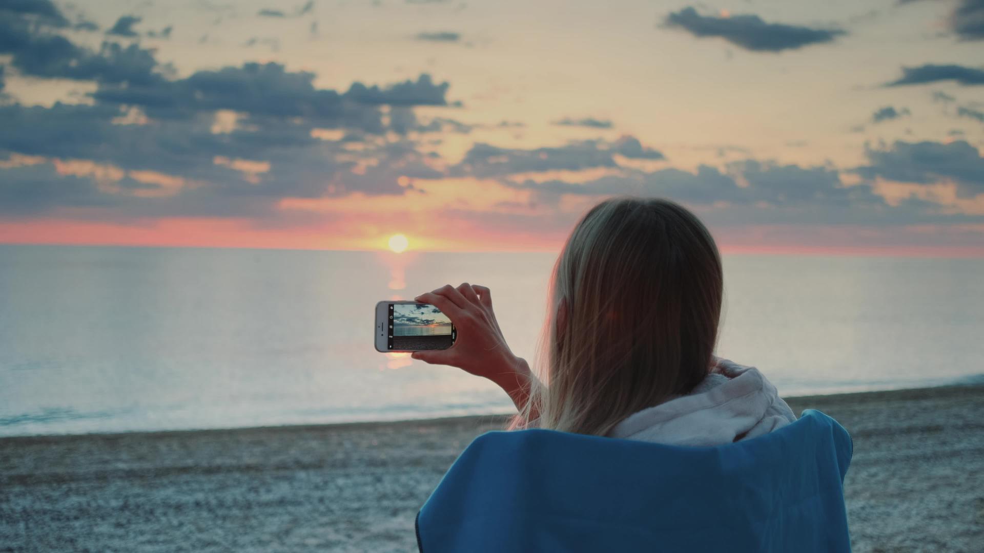 女性拍摄日落视频智能手机坐在海边视频的预览图