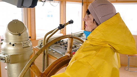 穿着黄色雨衣的老年妇女控制着船舵视频的预览图