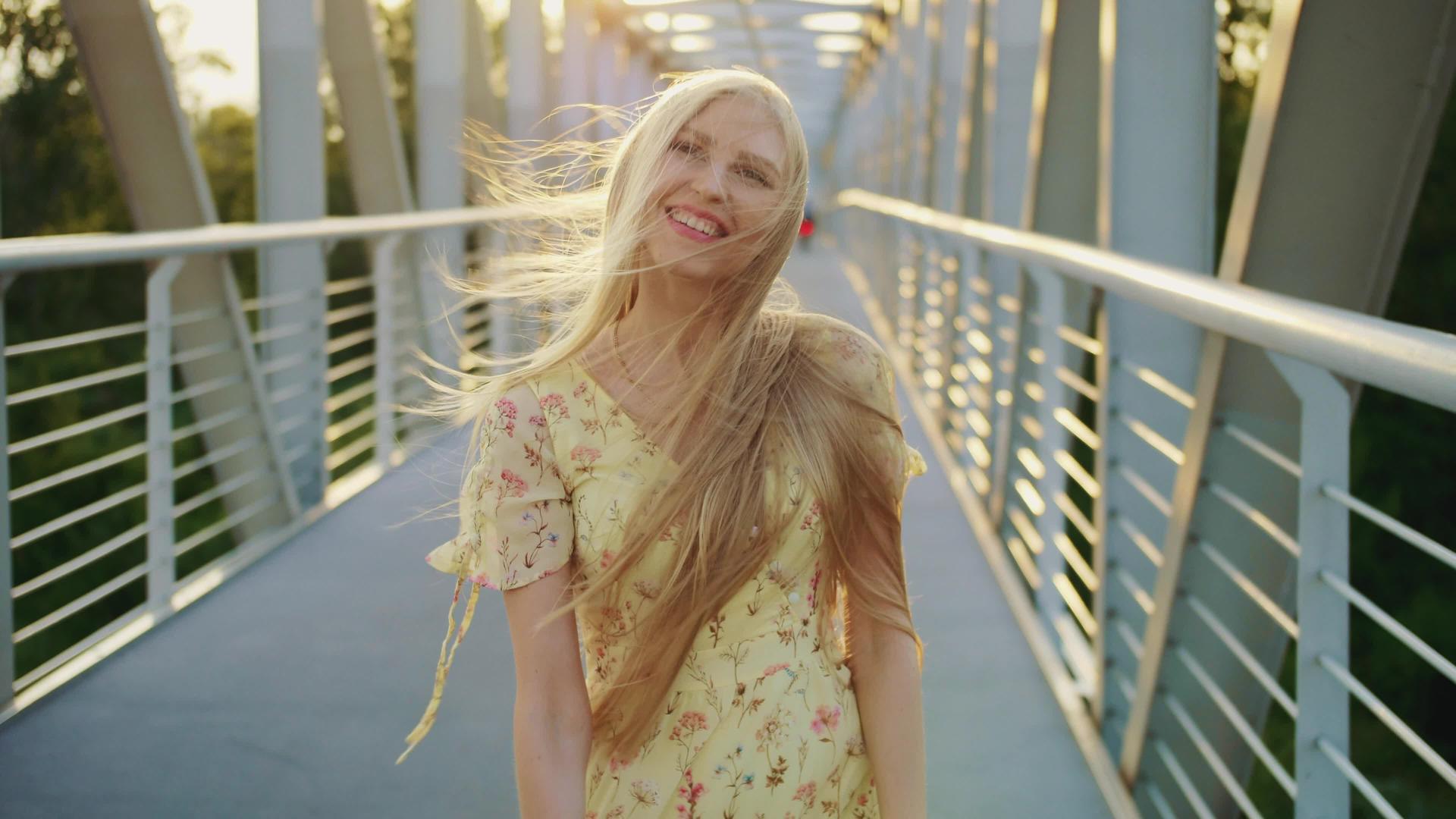 这位美丽的金发年轻女士看着相机一边在桥上跑一边卷曲视频的预览图
