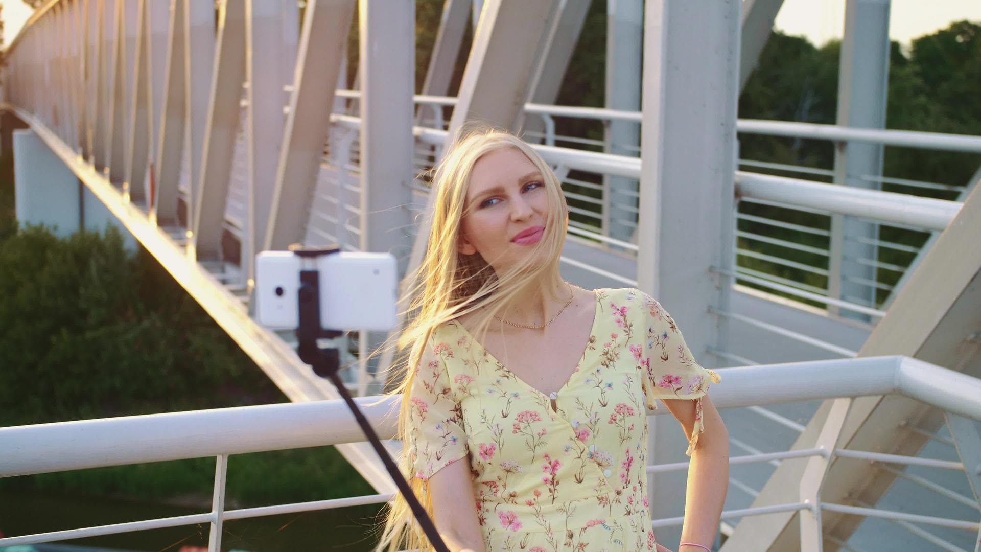 快乐的金发美女站在行人桥上日落时与独角兽一起拍摄视频的预览图
