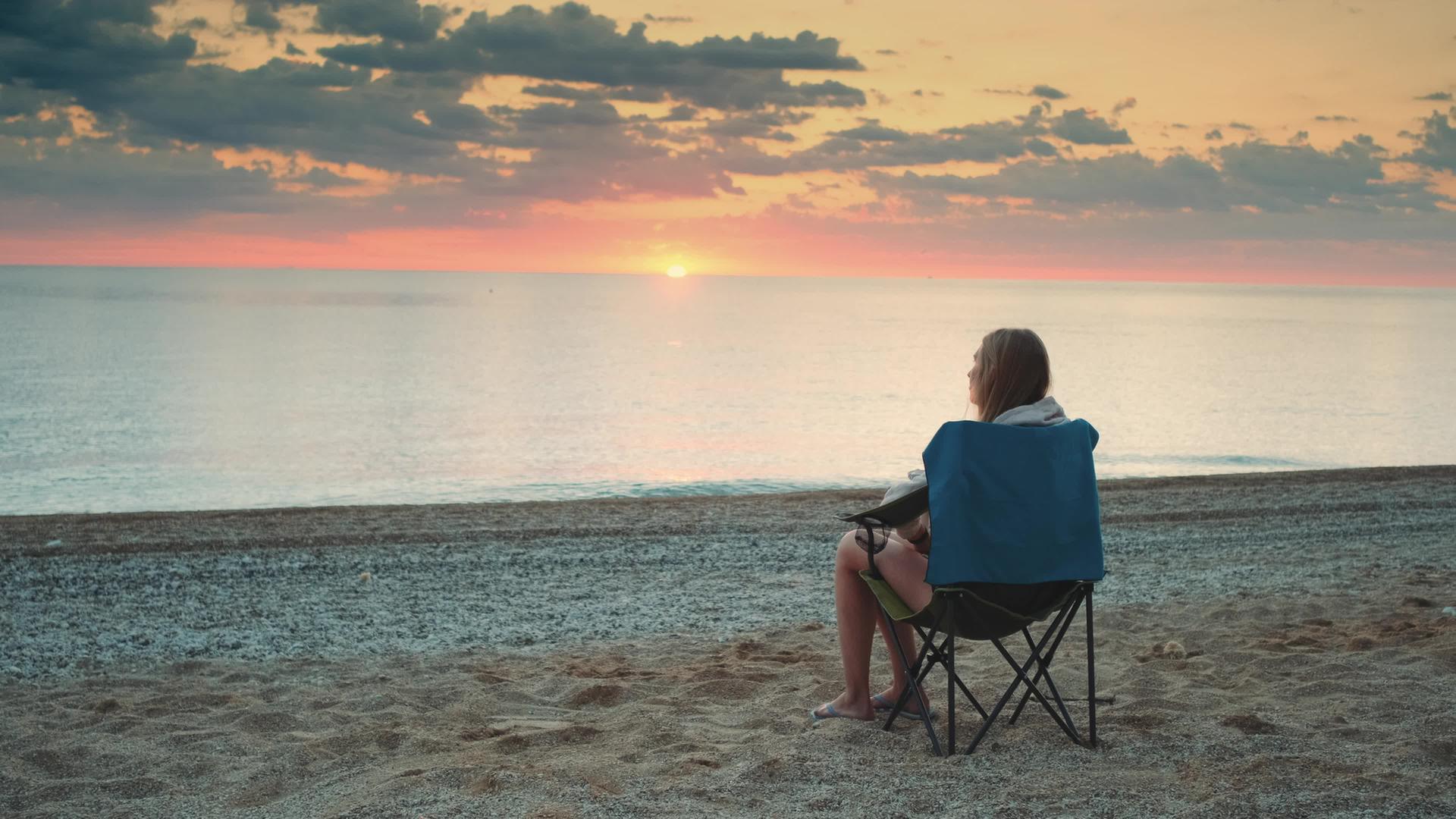 海边的女人坐在折叠的旅游椅上享受日落视频的预览图
