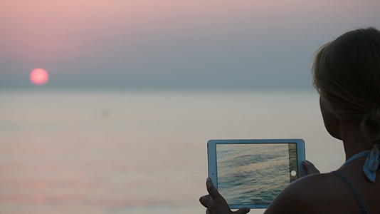 女性使用平板电脑制作日落照片视频的预览图