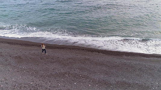 年轻女性在海边行走随波逐流观察无人机沿着模型飞来飞去视频的预览图