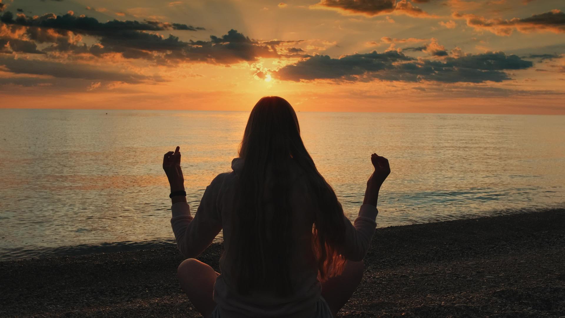 一个女人滩上做瑜伽冥想姿势的女人的背影视频的预览图
