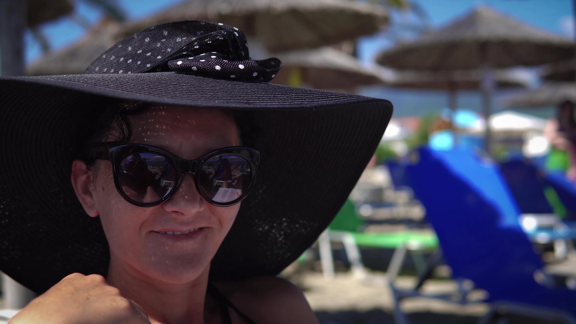 美丽的美女戴着帽子坐在沙滩度假胜地微笑着视频的预览图