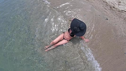 一个性感迷人的美女戴着草帽坐在海滩上享受假期视频的预览图