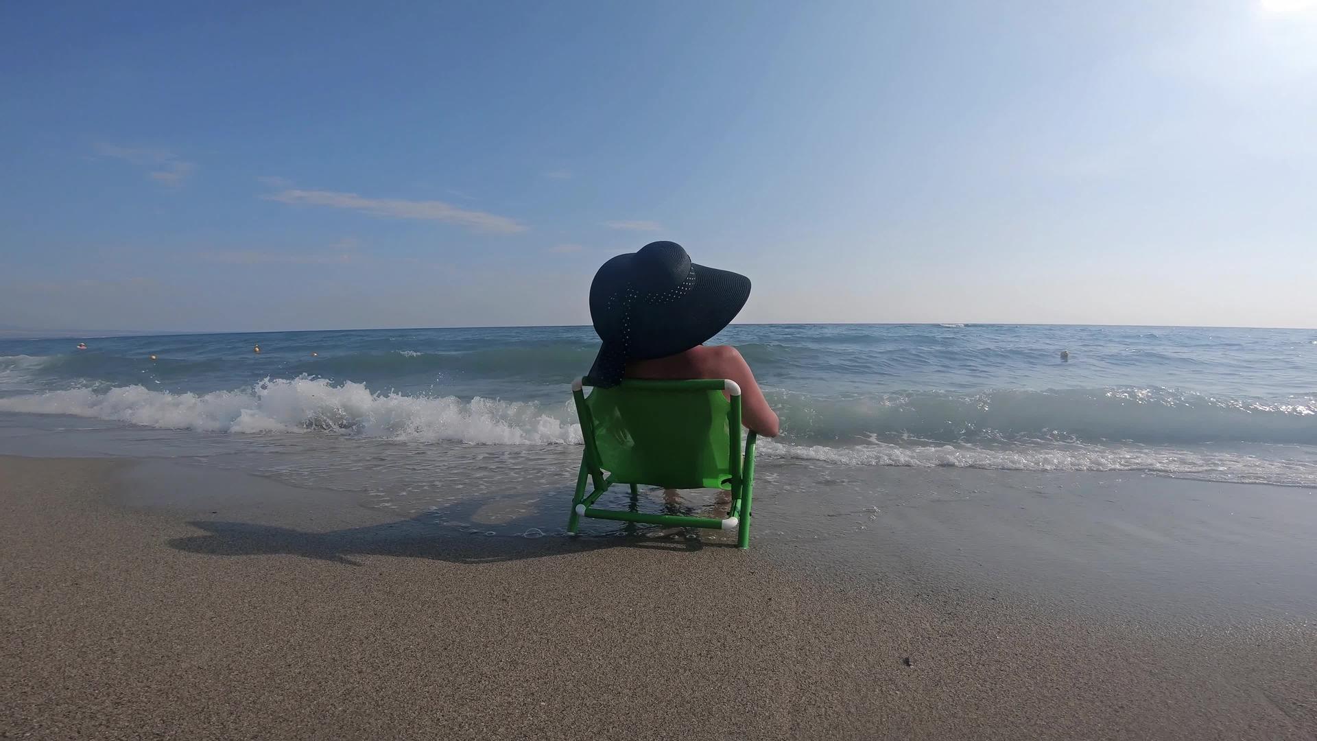 穿着比基尼的迷人女人坐在岸边喝咖啡戴着草帽放松视频的预览图