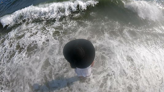 一个戴着草帽的女人在海边散步享受假期在空中看着她视频的预览图