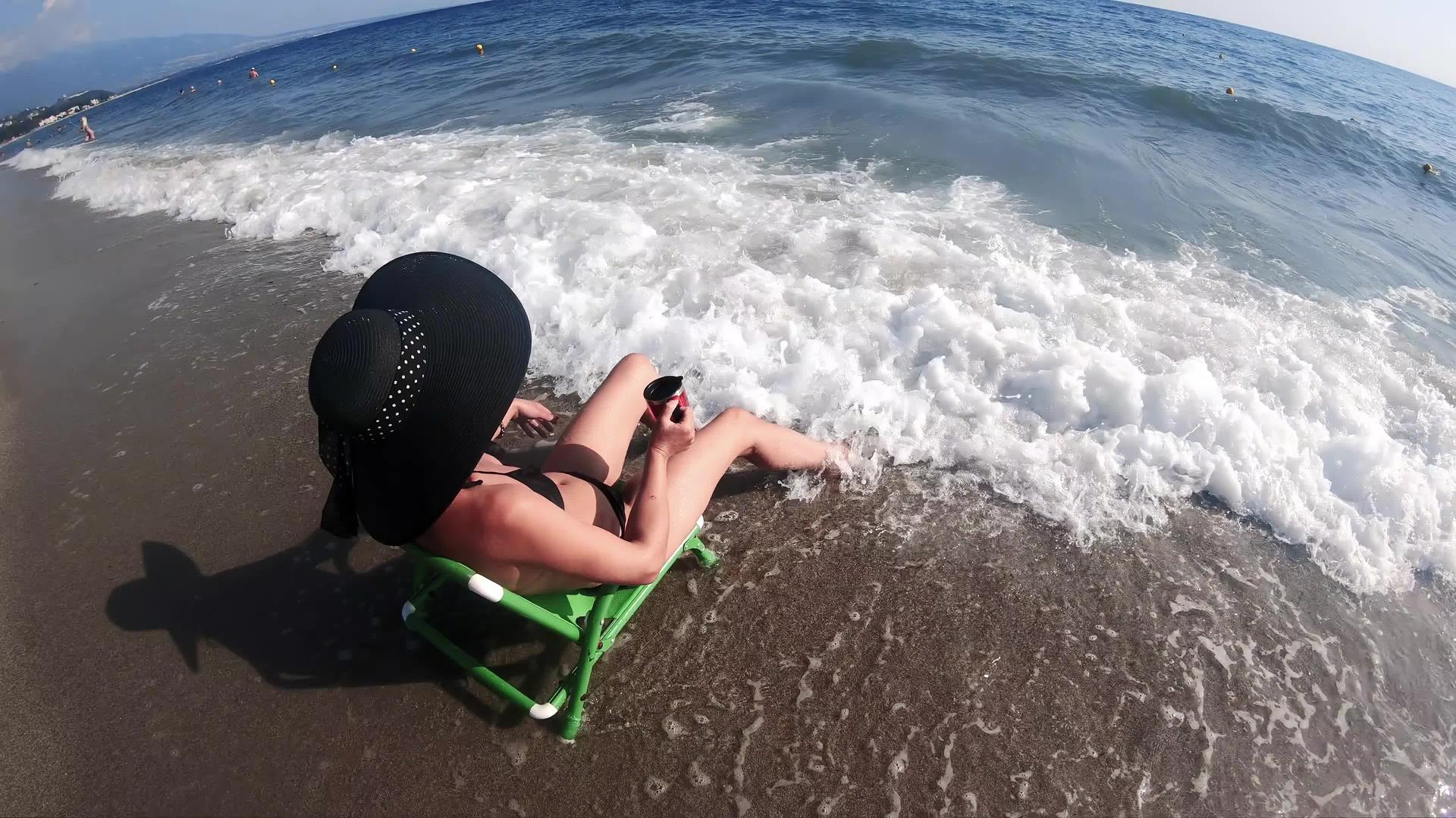 一个戴着草帽的漂亮女人慢慢地坐在沙滩上她的腿在沙滩上视频的预览图