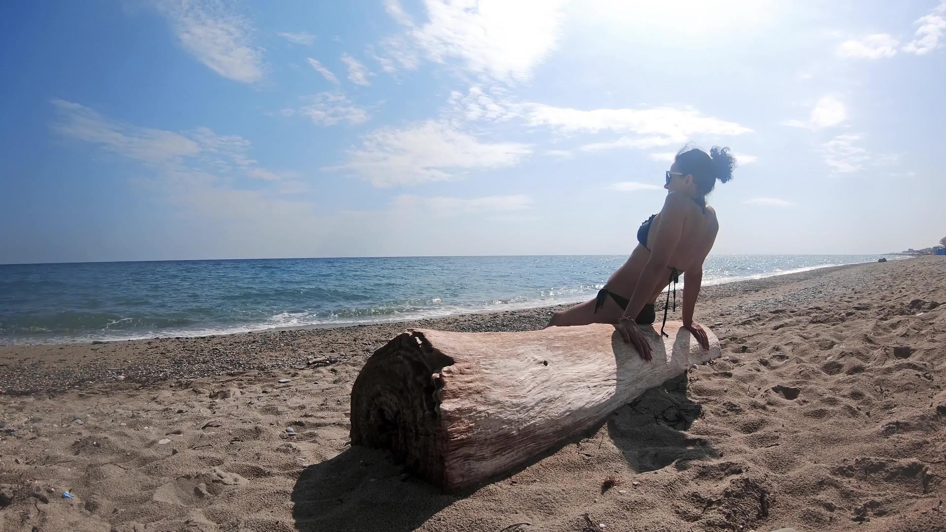 一位年轻女士坐在热带海滩的树干上慢慢地移动视频的预览图