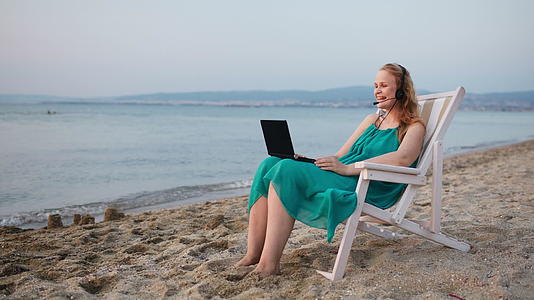 女人在沙滩上放松她用笔记本电脑说话视频的预览图
