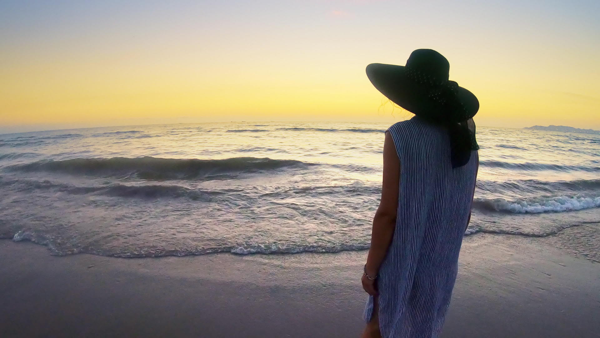 日落时在热带海滩上赤脚穿衣服戴帽子视频的预览图
