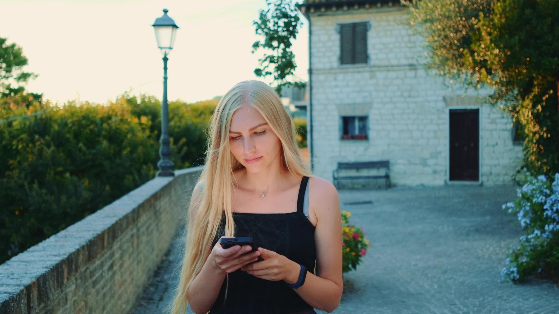 迷人的年轻女性在夏天外出时使用智能手机视频的预览图