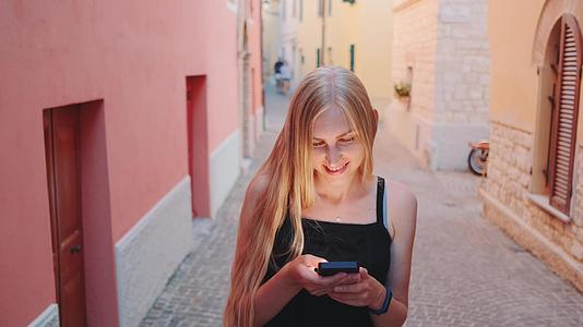 漂亮的金发美女在街上散步时在智能手机上聊天视频的预览图