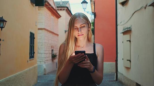 金发女在街上散步时在智能手机上读书视频的预览图