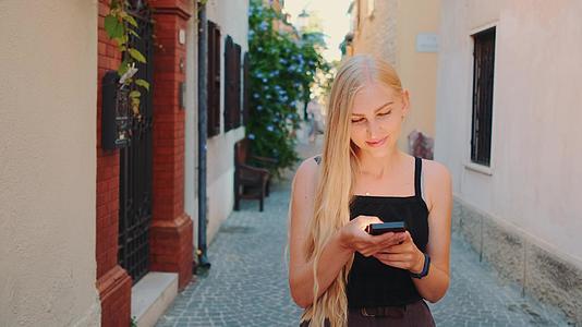 漂亮的金发美女在街上散步时在智能手机上聊天视频的预览图