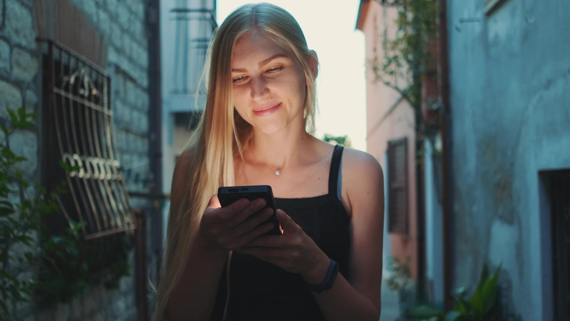在街上行走时一名金发女子正在使用智能手机视频的预览图