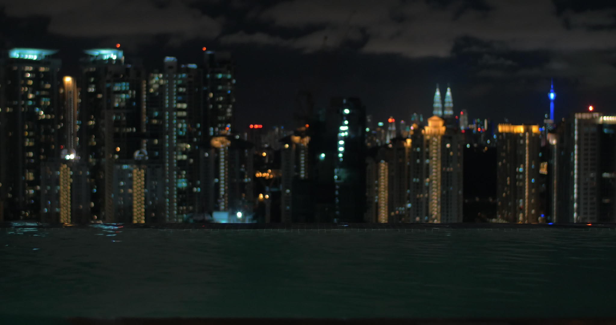 在摩天大楼屋顶的游泳池中女性与马拉西亚的城市夜景相对视频的预览图