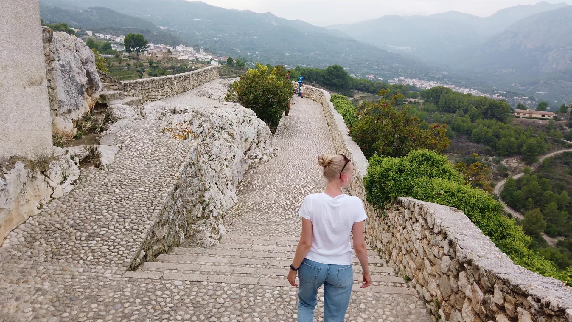 金发女子走在欧洲山中中世纪城堡的防御墙上视频的预览图
