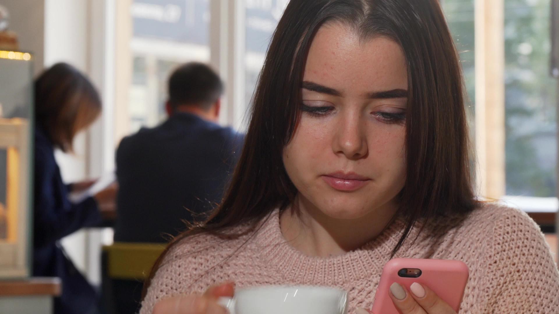 一个迷人的女人在咖啡馆里用智能手机喝咖啡使用她的智能手机视频的预览图