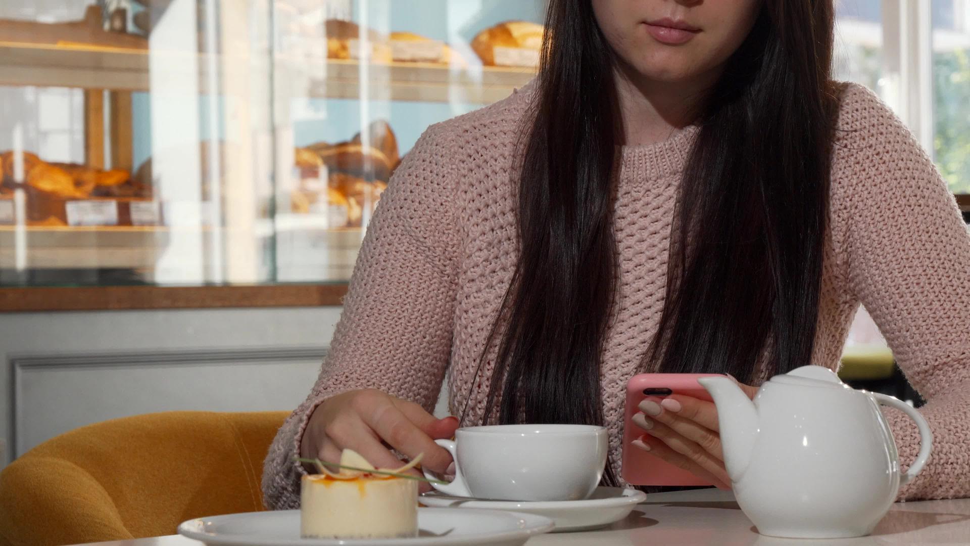 不知名的女性在咖啡店喝热茶时使用智能手机视频的预览图