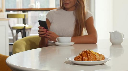 在面包店和咖啡馆使用智能手机的女性甜羊角面包视频的预览图