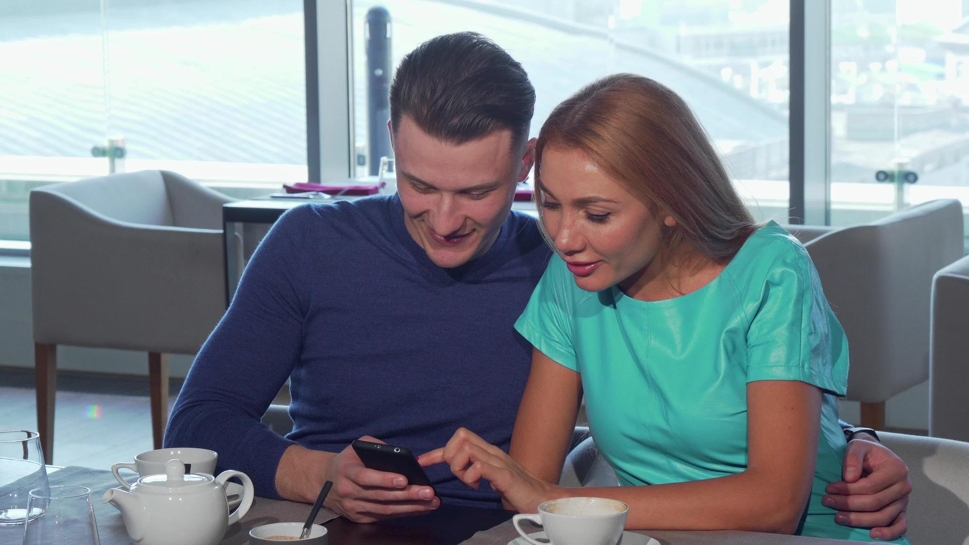 快乐的情侣拥抱在咖啡馆里一起使用智能手机视频的预览图