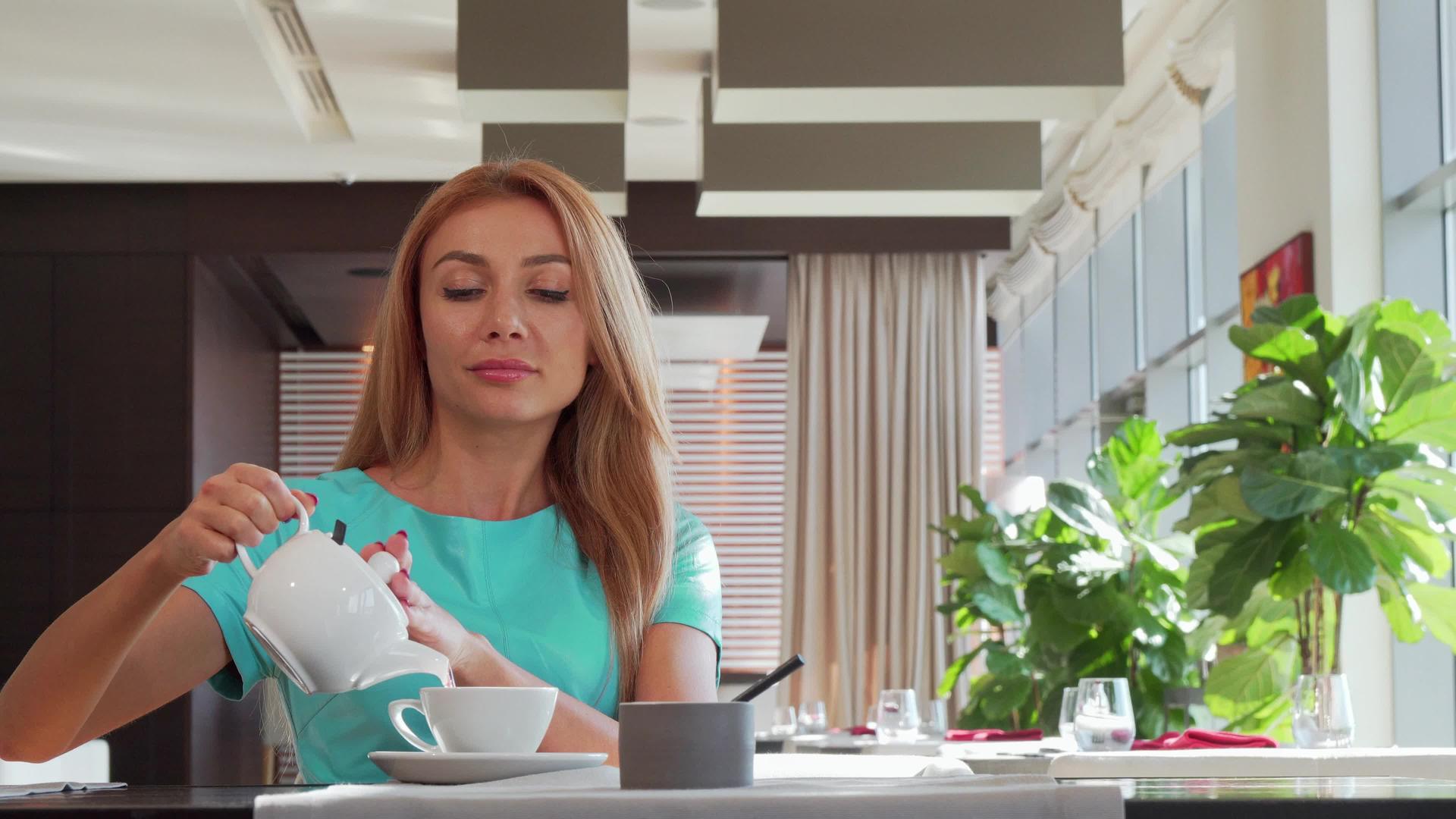美丽快乐的女人在茶杯里倒茶享受餐厅的早餐视频的预览图