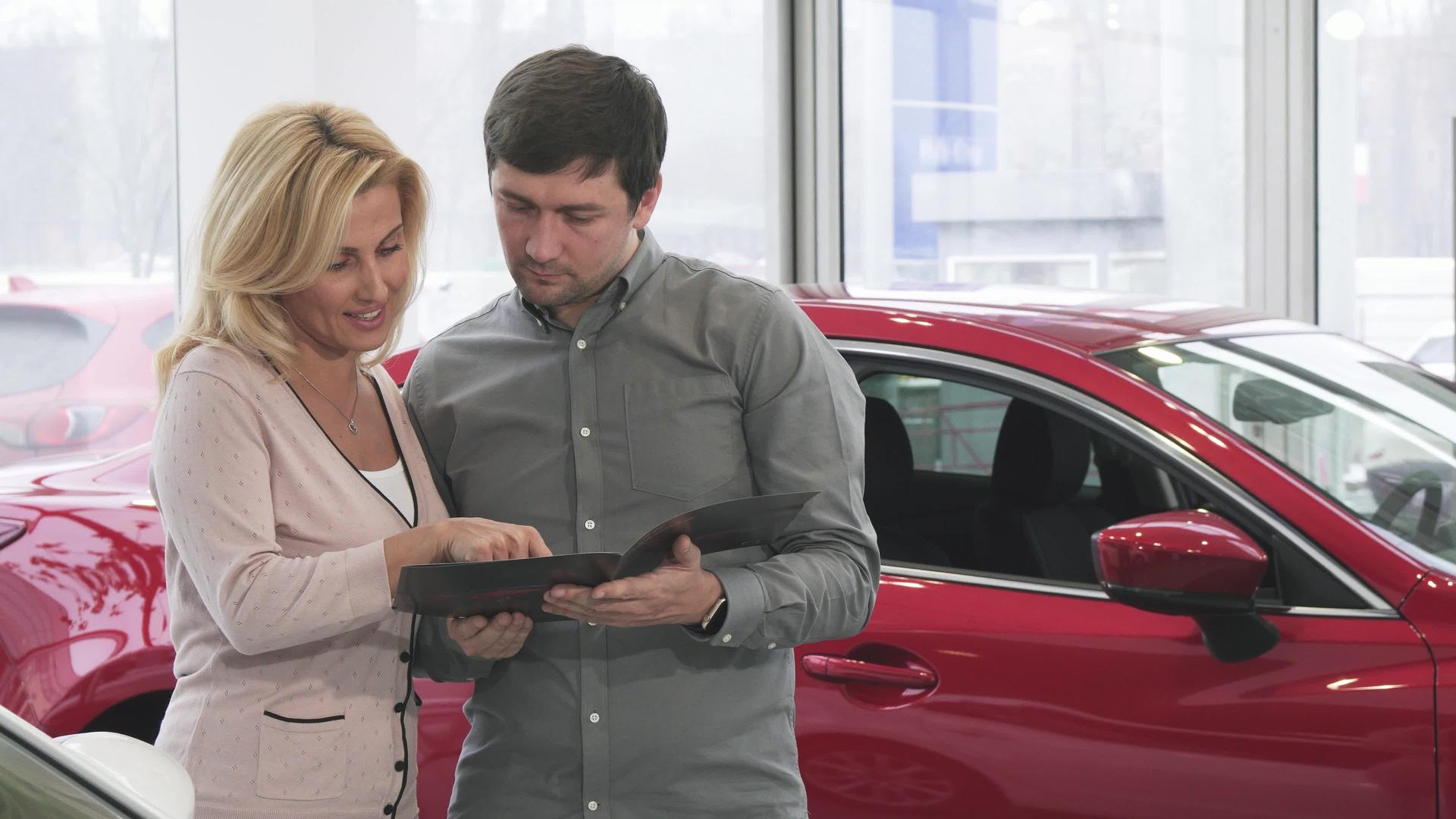 成年夫妇在汽车经销商购买新车时阅读小册子视频的预览图
