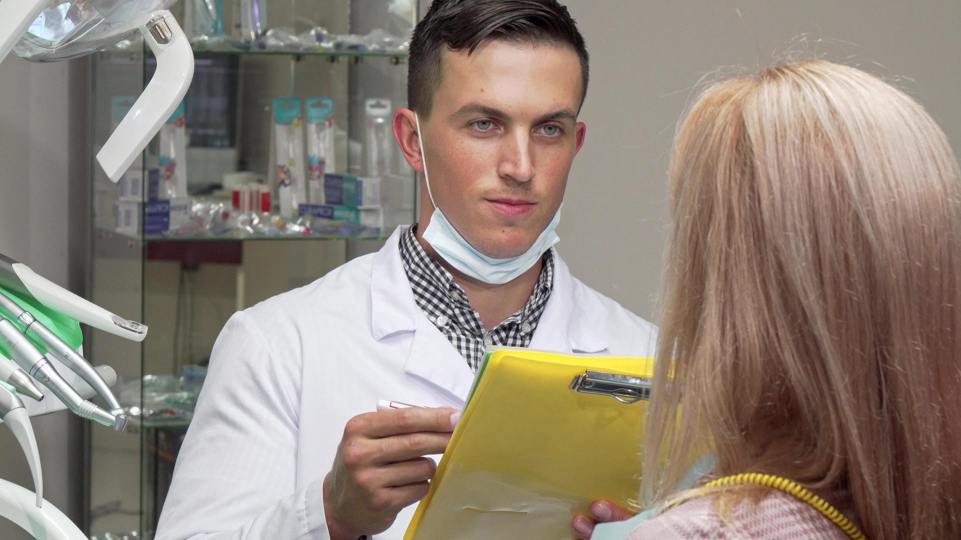 年轻男性牙医与女性患者交谈检查医疗文件；男性牙医视频的预览图