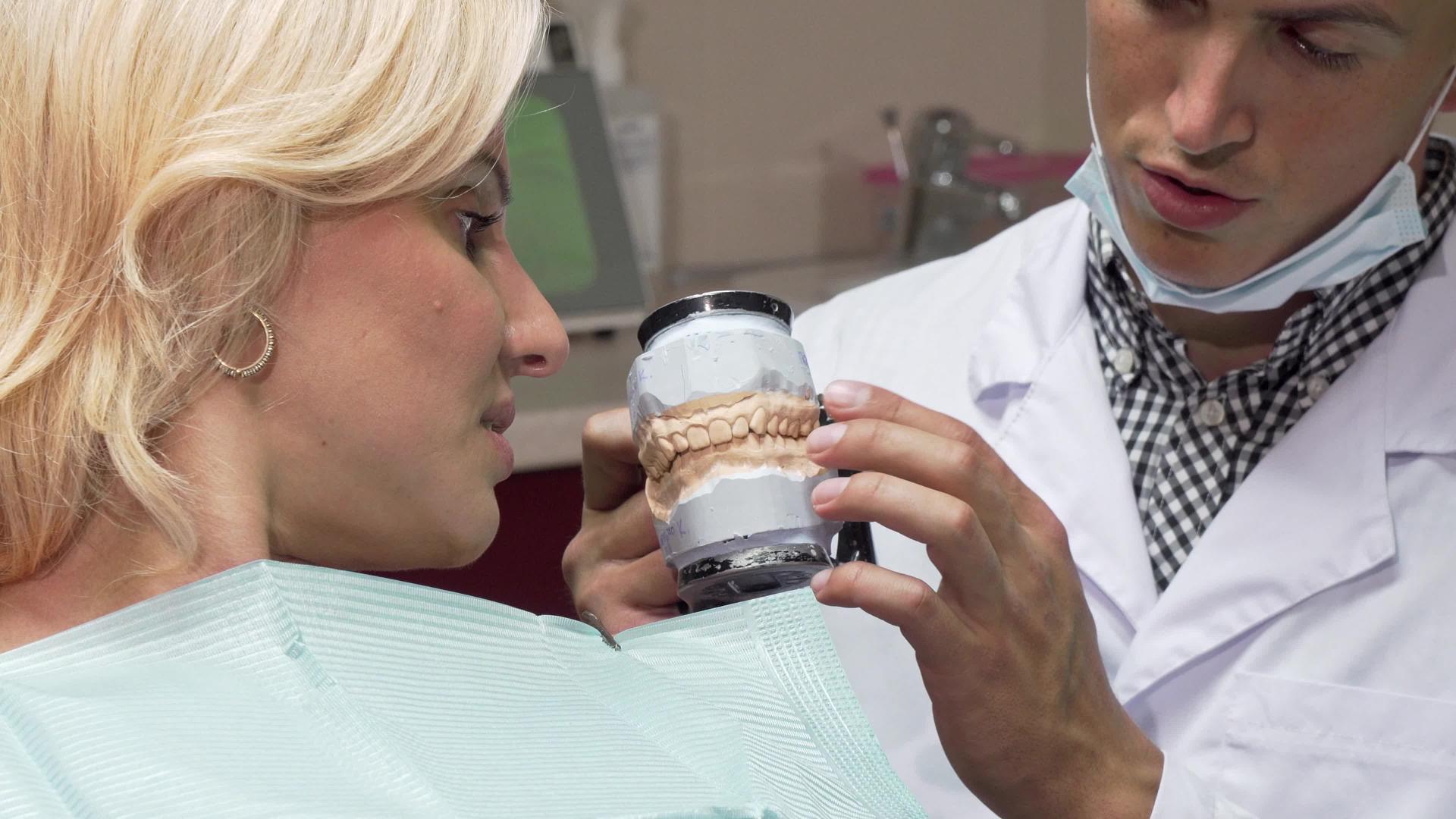 在他的诊所工作的男性牙医向患者展示了牙科模具；和视频的预览图