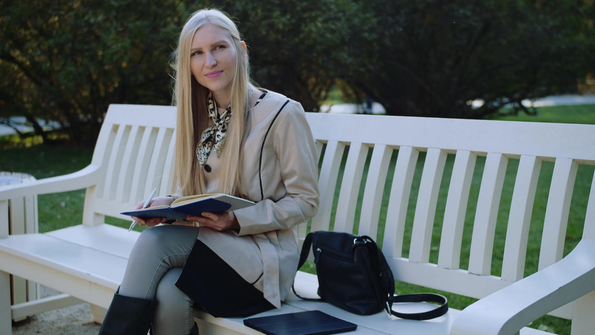 美丽的女人坐在秋天公园的长椅上做笔记视频的预览图