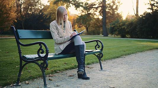 美丽的年轻女子在公园户外写日记在公园写日记视频的预览图