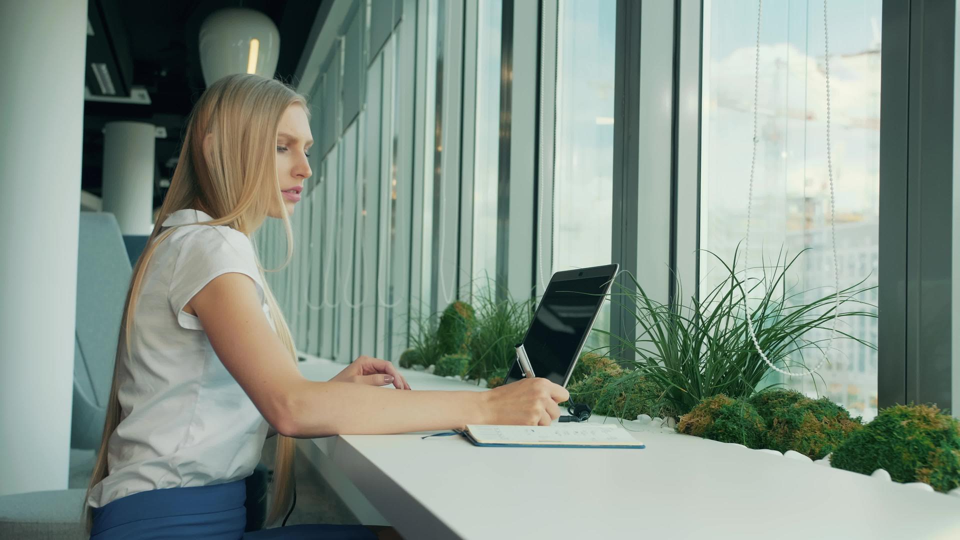 在现代办公室的窗户附近盖电脑和文件的正式女性视频的预览图
