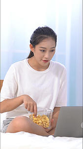 女生边吃爆米花边看电脑竖构图视频视频的预览图
