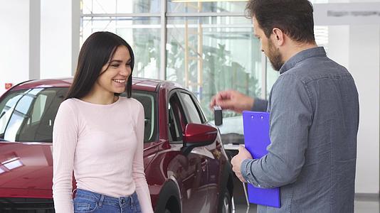 收到车钥匙后美丽快乐的女人与汽车经销商握手视频的预览图