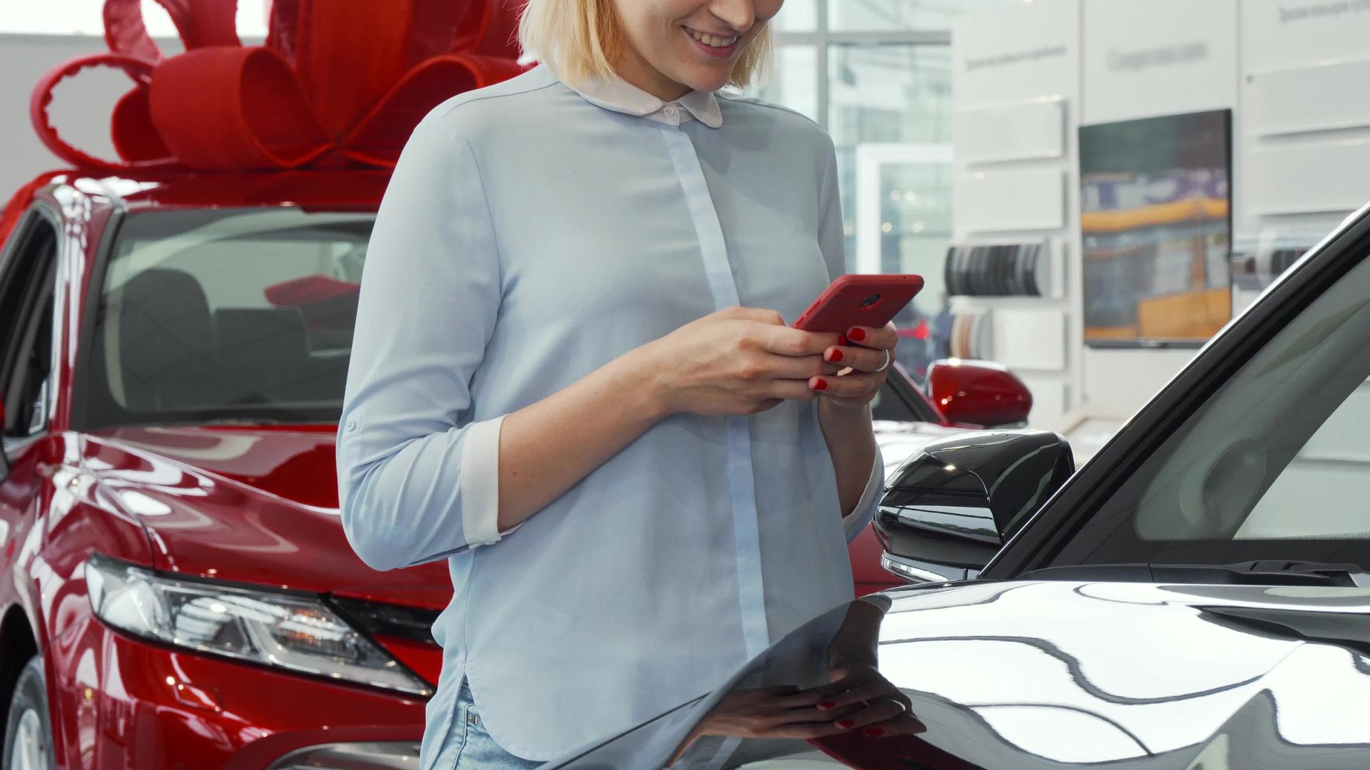 女性在汽车经销商店使用智能手机视频的预览图
