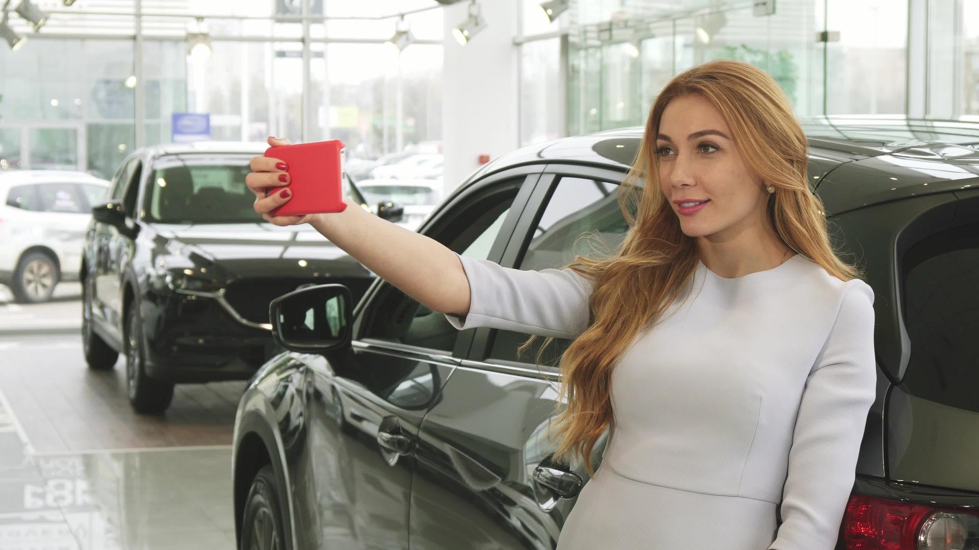 美丽快乐的女人在经销商的新车旁边自拍视频的预览图