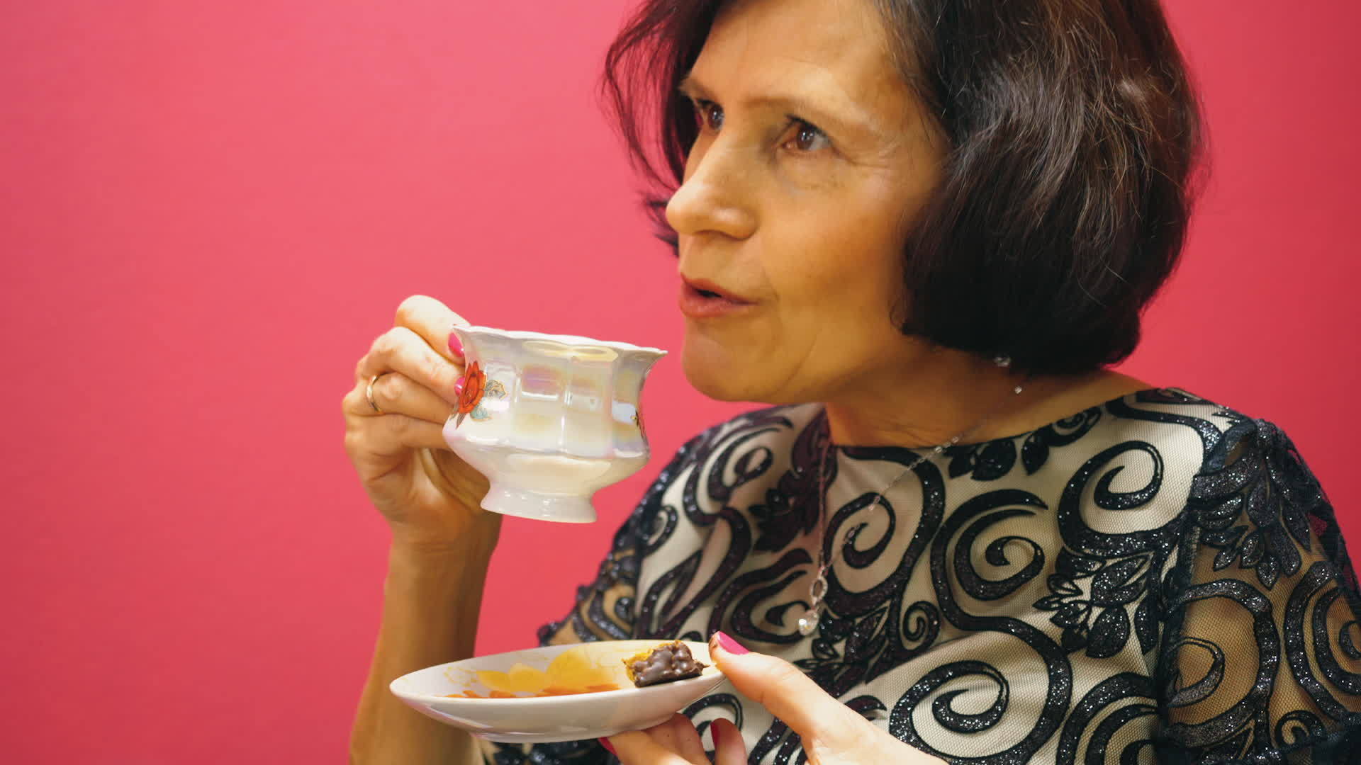年长的黑发女人在红色的背景下喝一杯茶吃糖果视频的预览图