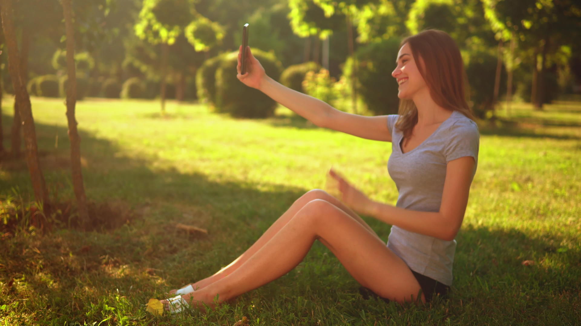 坐在公园草坪上的女性使用智能手机视频的预览图